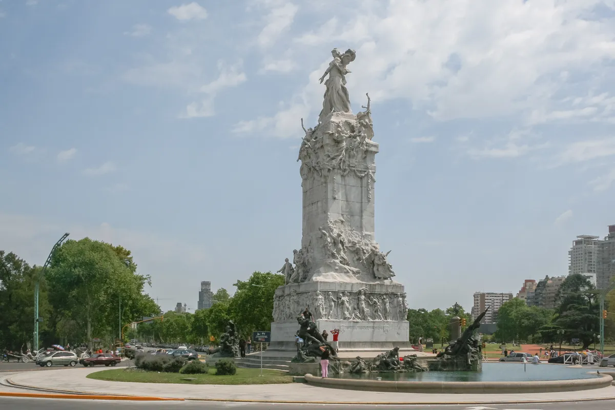 El Monumento de los Españoles, una gran estructura de piedra blanca con grupos escultóricos de bronce en su base, en medio del cruce de avenidas arboladas de Palermo.