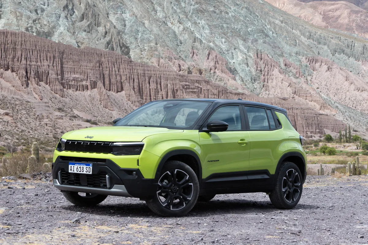 Un Jeep Avenger verde de tres cuartos de frente, ante cerros estriados de varios colores.