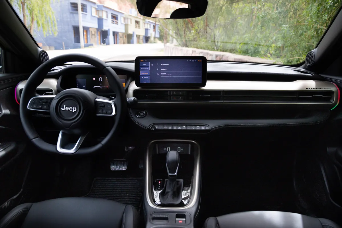 Vista amplia del interior de un Jeep Avenger: volante con comandos, tablero digital y pantalla central sobre un tablero negro con detalles plateados.