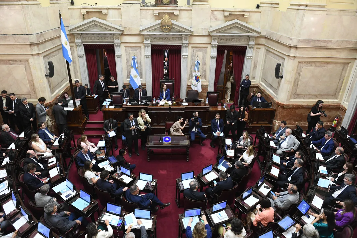 El recinto del Senado de la Nación visto desde lo alto, con las bancas en semicírculo frente al estrado de la presidencia y banderas argentinas.