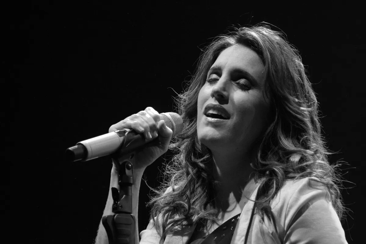 Soledad Pastorutti, con el pelo largo y ondulado y un saco claro, canta con los ojos cerrados aferrada al micrófono, en una foto en blanco y negro sobre fondo oscuro.