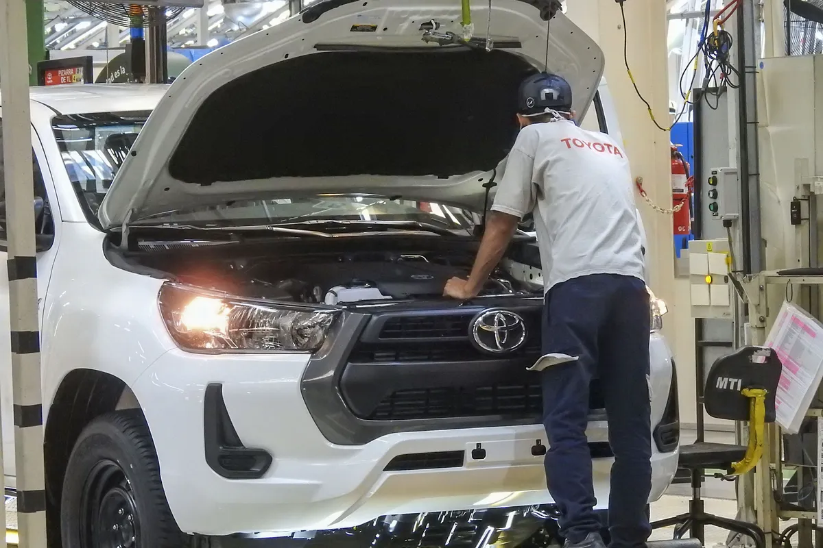 Un operario con remera gris de Toyota se inclina sobre el vano motor abierto de una Hilux blanca en la planta de Zárate.